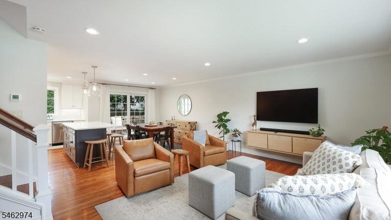 Open-plan living room with leather armchairs, hardwood floors, and a large television beside the dining area and kitchen.