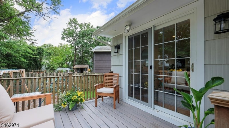 Deck with cushioned seating, potted flowers, and sliding glass doors overlooking a fenced yard.