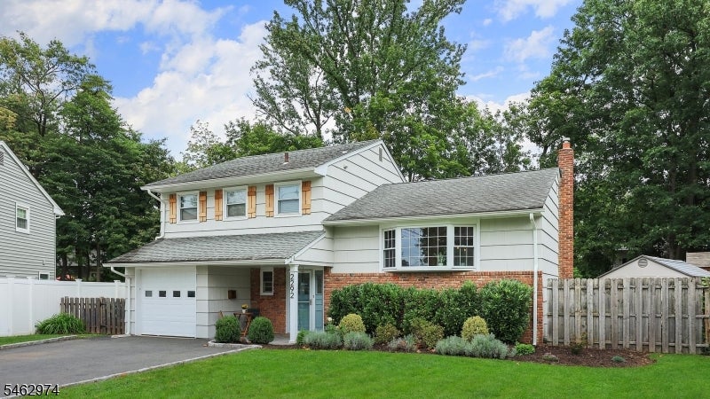 Two-story white-sided home with brick accents, an attached garage, and a landscaped front lawn.