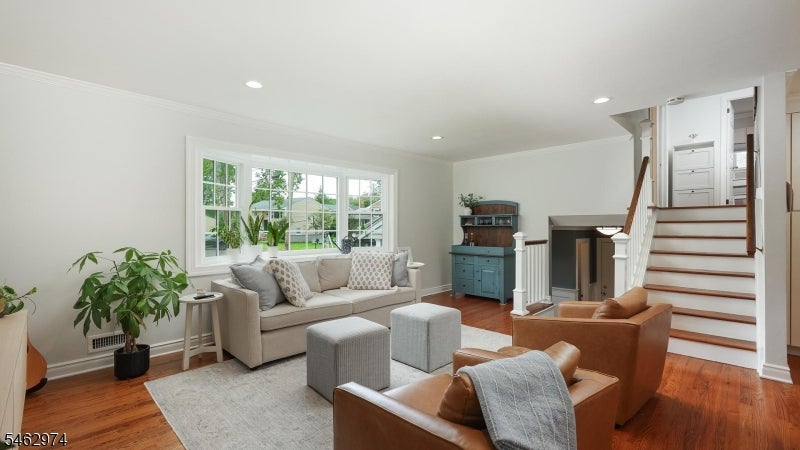 Living room with a large window, hardwood floors, leather armchairs, and a staircase beside the fireplace.