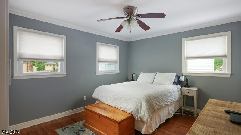 Bedroom with a white bed, gray walls, three windows, and a wooden chest at the foot of the bed.