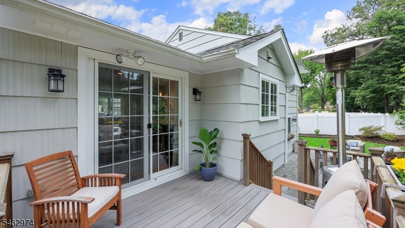 Raised deck with gray flooring, wooden chairs, a patio heater, and sliding glass doors.