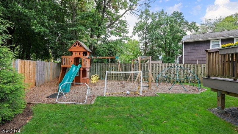 Fenced backyard with a wooden playset, teal slide, swings, and climbing dome.