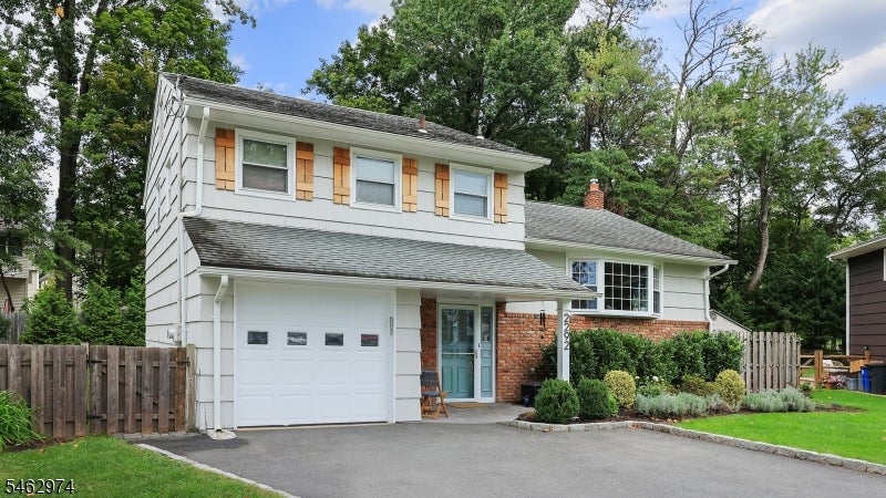 Split-level house with white siding, brick accents, an attached garage, and a paved driveway.