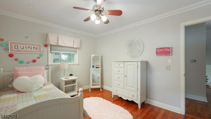 Child’s bedroom with a white bed, pink heart pillow, and white dresser on hardwood floors.