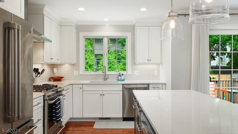 White kitchen with a large quartz island, stainless steel appliances, and windows overlooking greenery.