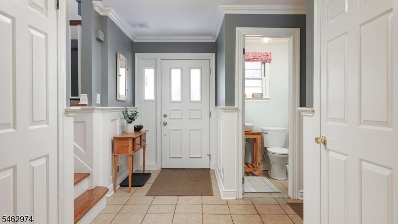 Entry foyer with tiled floors, white wainscoting, a wooden console table, and a bathroom doorway.