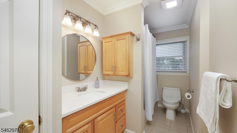 Bathroom with a light wood vanity, round mirror, toilet, and window with blinds.