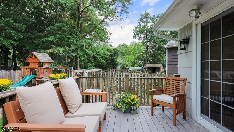 Backyard deck with cushioned wooden seating overlooking a fenced yard and children's playset.