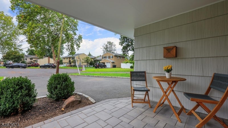 Covered porch with wooden seating and a small table overlooking a tree-lined residential street.