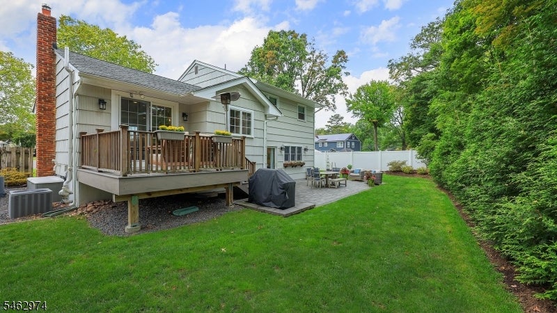 Backyard with raised wooden deck, broad lawn, patio seating, and tall evergreen hedge.