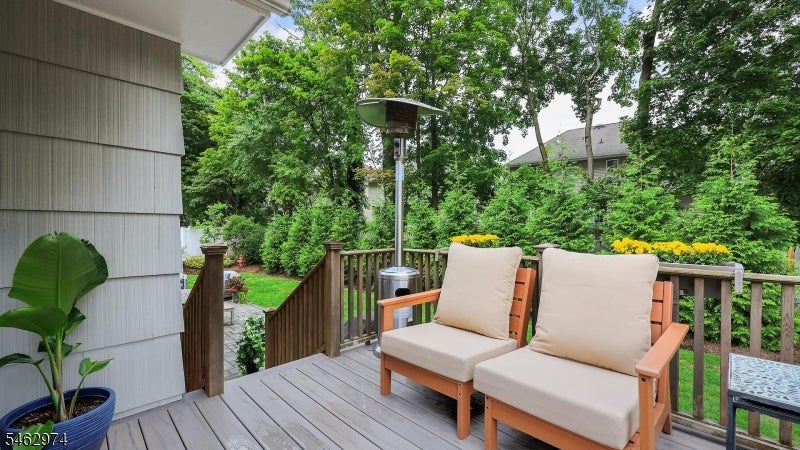 Backyard deck with two cushioned chairs and a patio heater, surrounded by leafy trees.