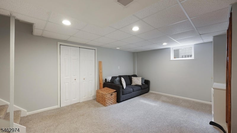 Finished basement living area with beige carpet, a dark sofa, and white closet doors.