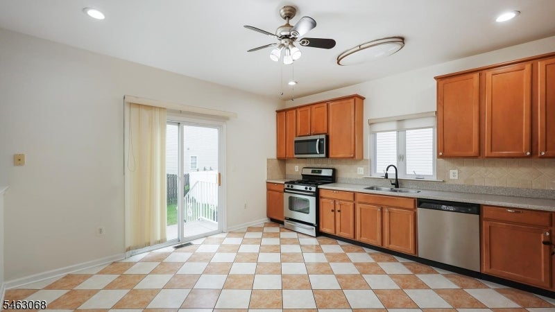 Kitchen with reddish wood cabinets, stainless steel appliances, checkerboard tile flooring, and a sliding glass door.