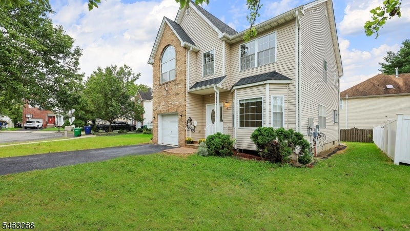 Two-story beige-sided house with brick facade, attached garage, driveway, and front lawn.