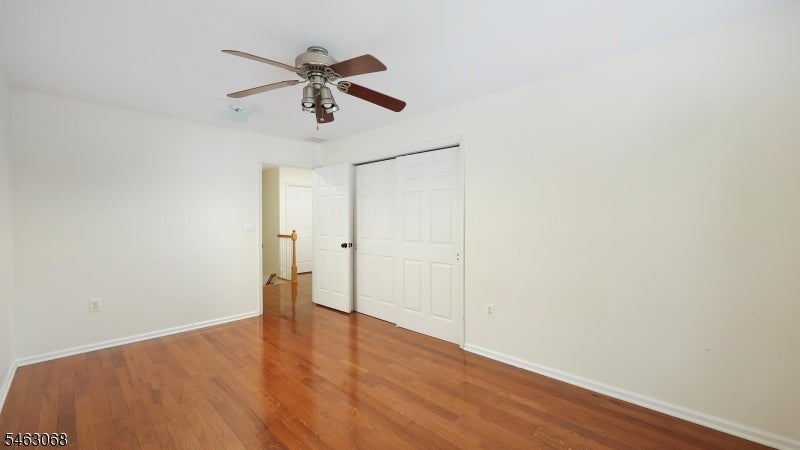 Empty bedroom with hardwood floors, white closet doors, and a ceiling fan.