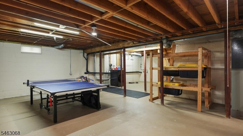 Basement recreation area with a ping-pong table, exposed ceiling joists, and wooden storage shelves.