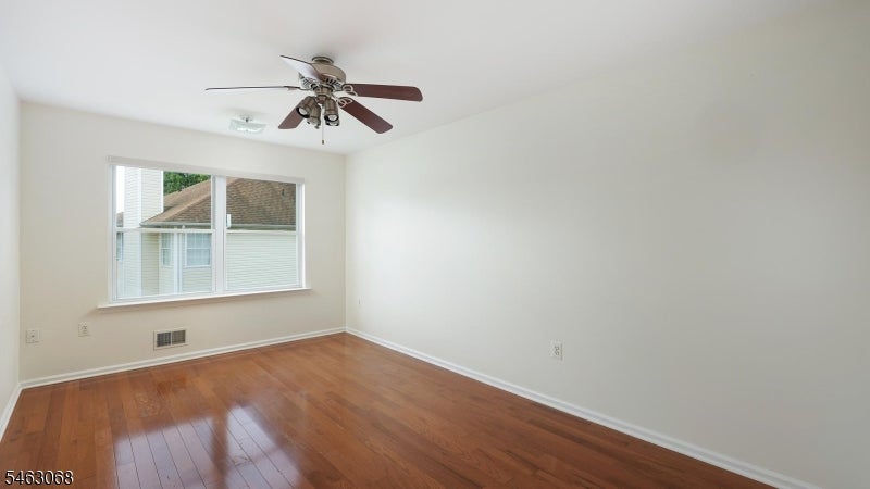 Empty room with polished hardwood floors, a large window, and a ceiling fan.
