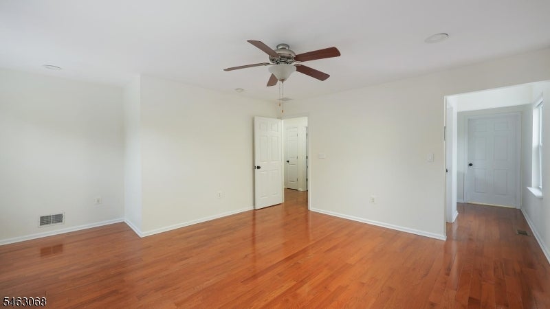 Empty room with polished hardwood floors and a ceiling fan, viewed toward two open doorways.