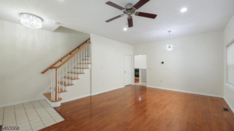 Vacant living area with hardwood floors, a staircase, and a tiled entry.