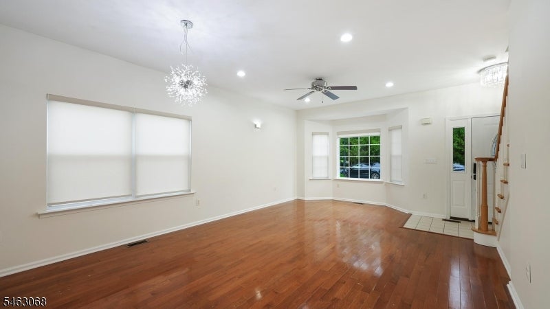 Vacant living and dining area with hardwood floors, bay window, chandelier, and staircase.
