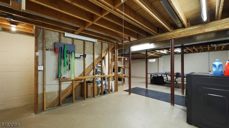 Unfinished basement with exposed ceiling joists, laundry appliances, and a table-tennis table.