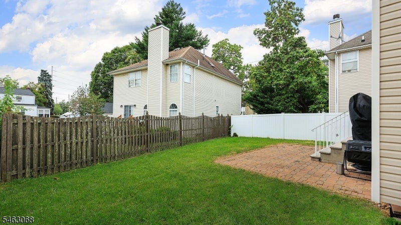 Backyard with a green lawn, brick patio, wooden fence, and covered grill.