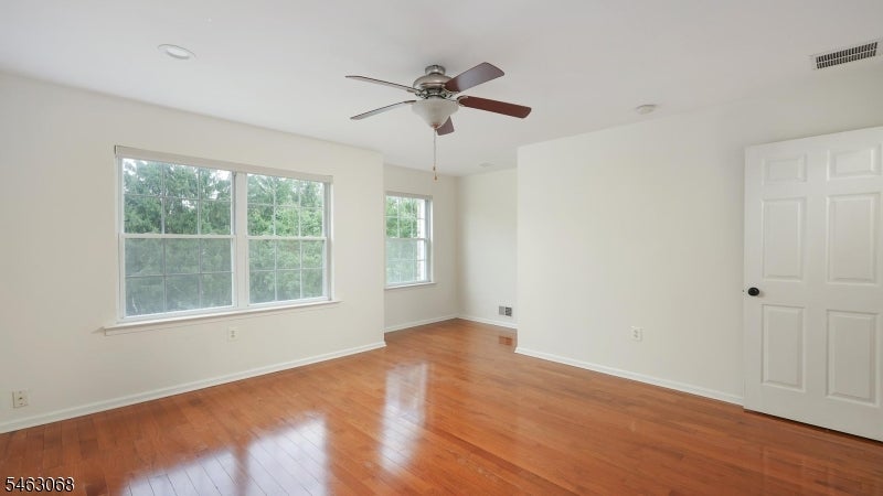 Empty room with polished hardwood floors, two windows, and a ceiling fan.