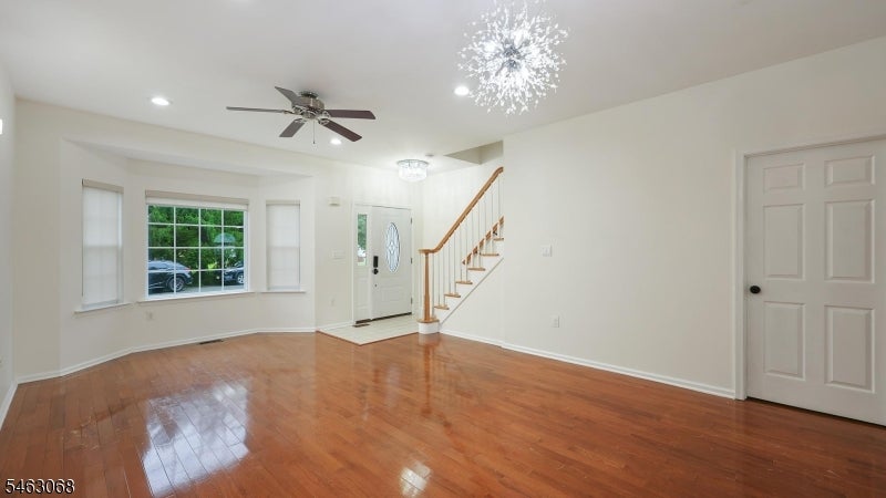 Empty entry room with glossy hardwood floors, front door, windows, and a wooden staircase.