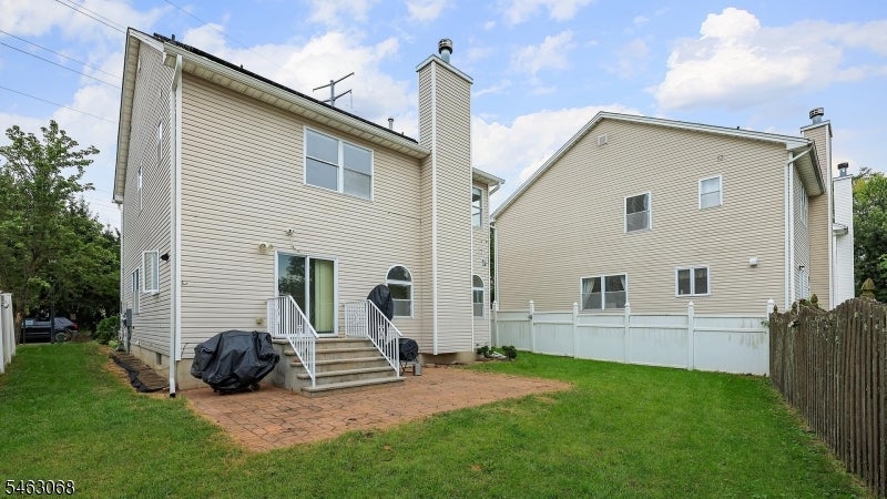 Rear exterior of a two-story beige-sided home with a brick patio, lawn, and fenced yard.