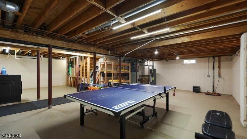 Basement recreation area with a ping-pong table, exposed ceiling beams, and exercise equipment.