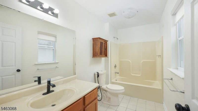 Bathroom with a cream tub and shower, wide vanity, and small wooden wall cabinet.