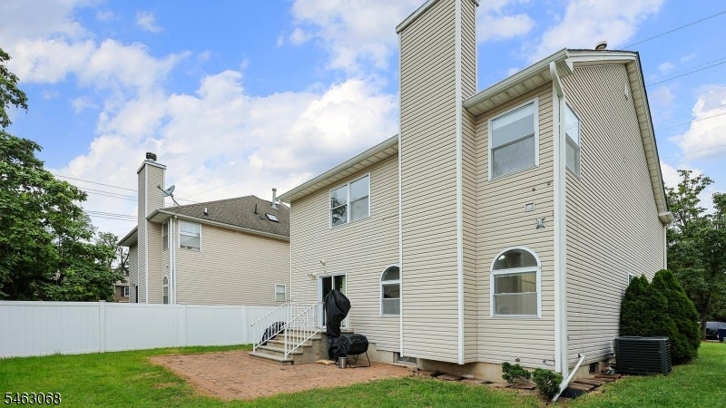 Rear exterior of a beige two-story house with arched windows, a brick patio, and white privacy fence.