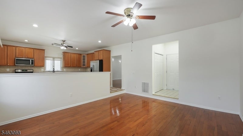 Empty living area with polished hardwood floors, an open kitchen, and ceiling fans.