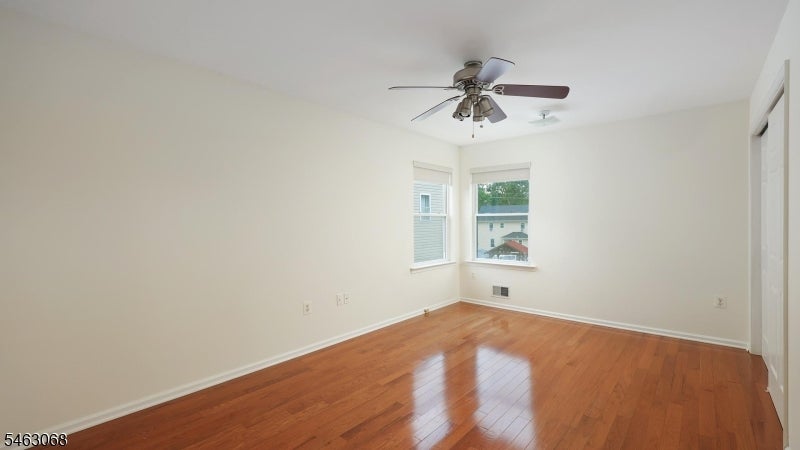 Empty room with hardwood floors, a ceiling fan, and two corner windows.