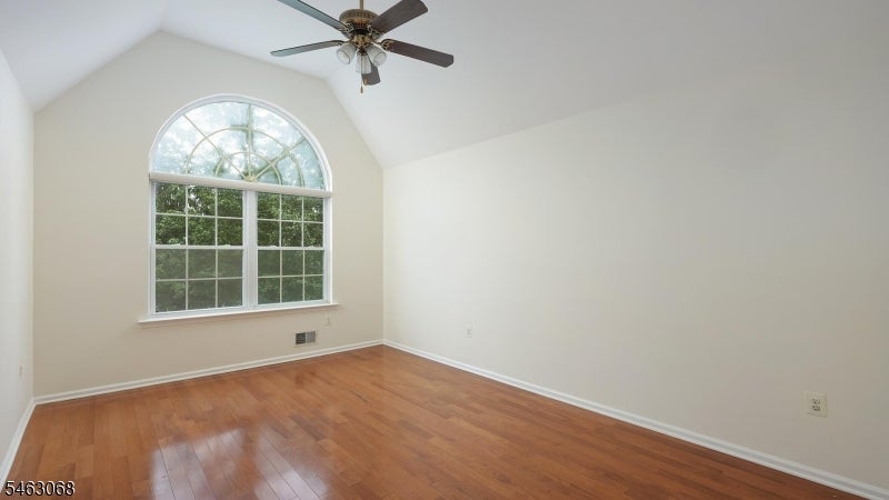 Empty bedroom with wood floors, a ceiling fan, and a large arched window.