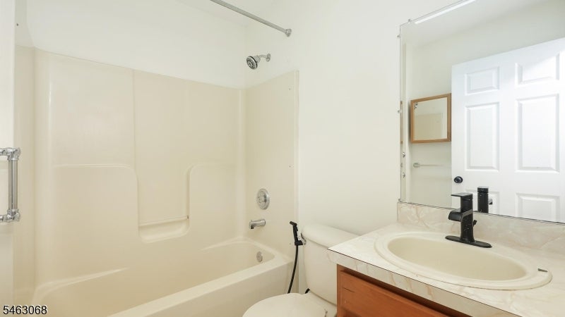 Bathroom with a cream tub and shower beside a wood vanity with an oval sink.