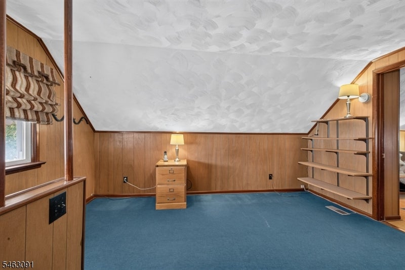 Empty wood-paneled room with blue carpet, built-in shelves, and a textured ceiling.