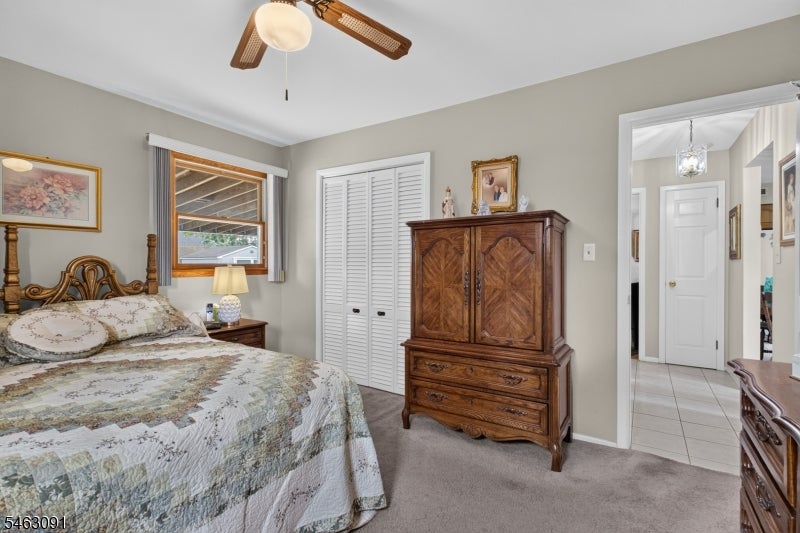 Bedroom with a patterned bedspread and carved wooden armoire beside an open doorway to a tiled hall.