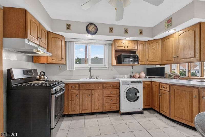 Kitchen with wood cabinetry, tiled floors, and a front-loading washer beside the sink.