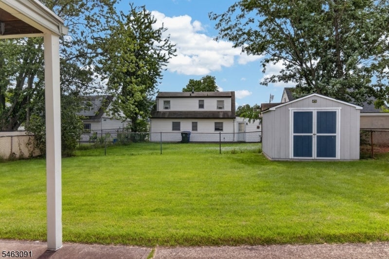 Backyard lawn with a white storage shed, chain-link fence, and neighboring house.