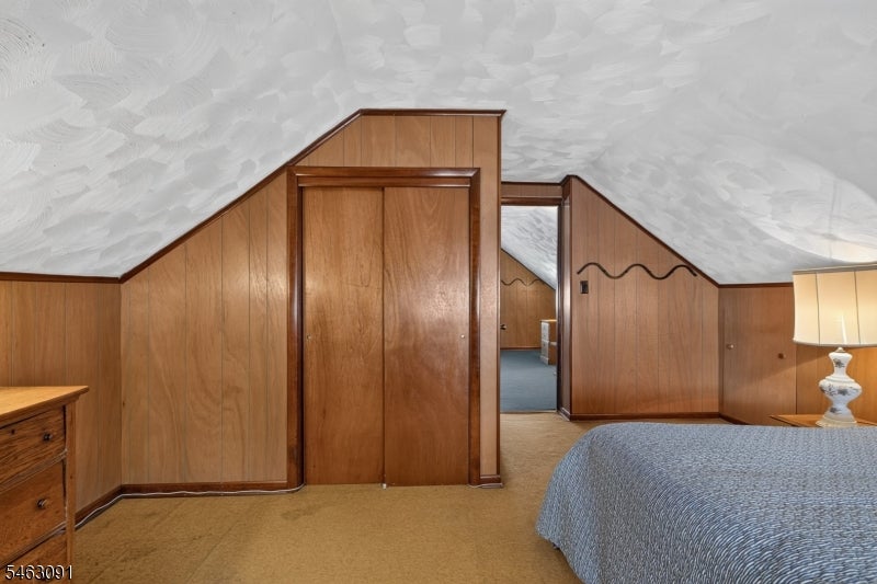Bedroom with wood-paneled walls, a sloped ceiling, and a doorway to an adjoining room.
