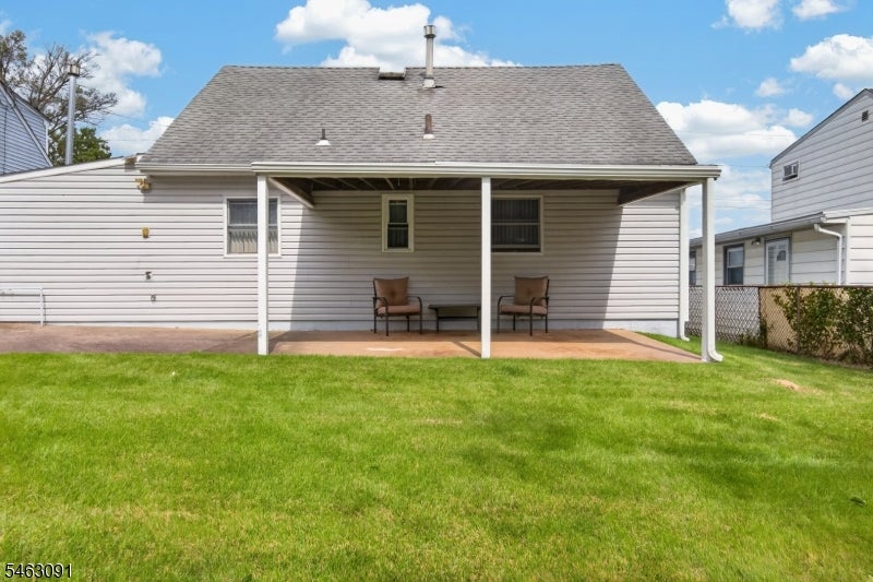 Rear of a white-sided home with a covered patio, two chairs, and a broad lawn.