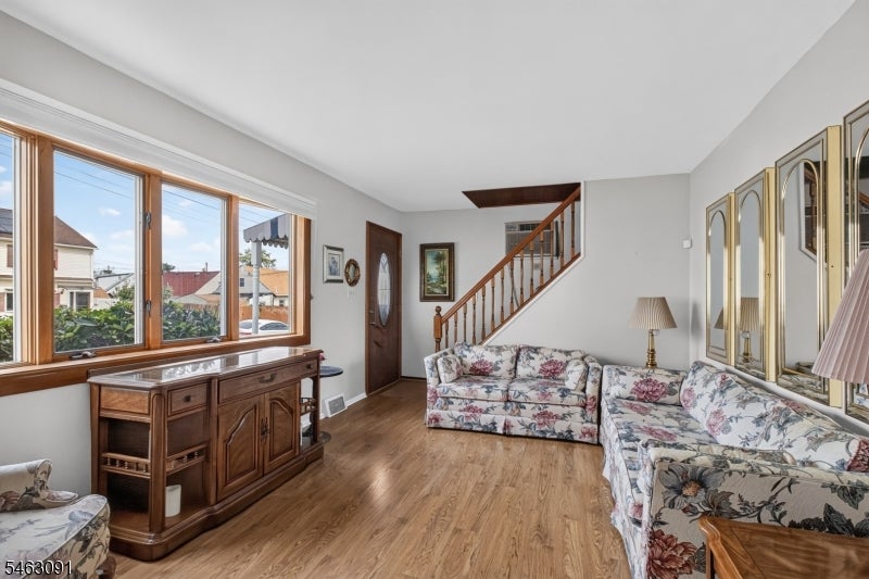 Living room with floral sofas, hardwood floors, and a staircase beside large windows.