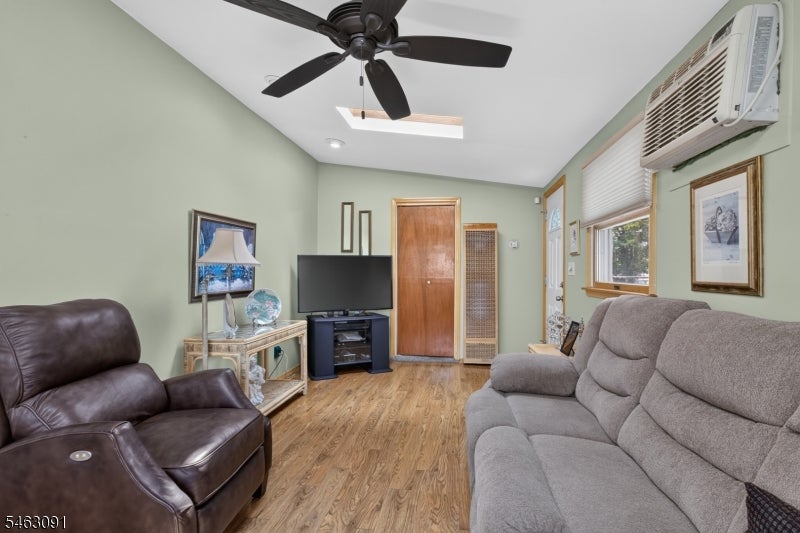 Living room with gray sofa, leather recliner, television, ceiling fan, and wall-mounted air conditioner.