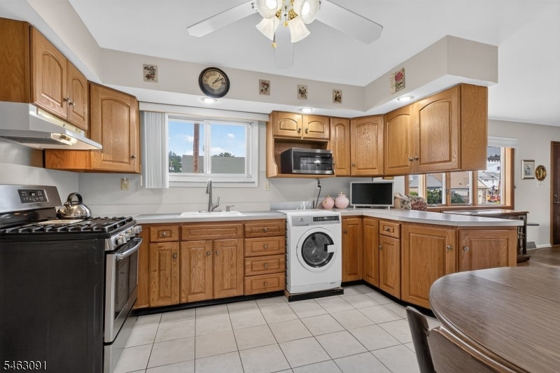 Kitchen with honey-colored wood cabinets, tiled floor, and a front-loading washing machine.