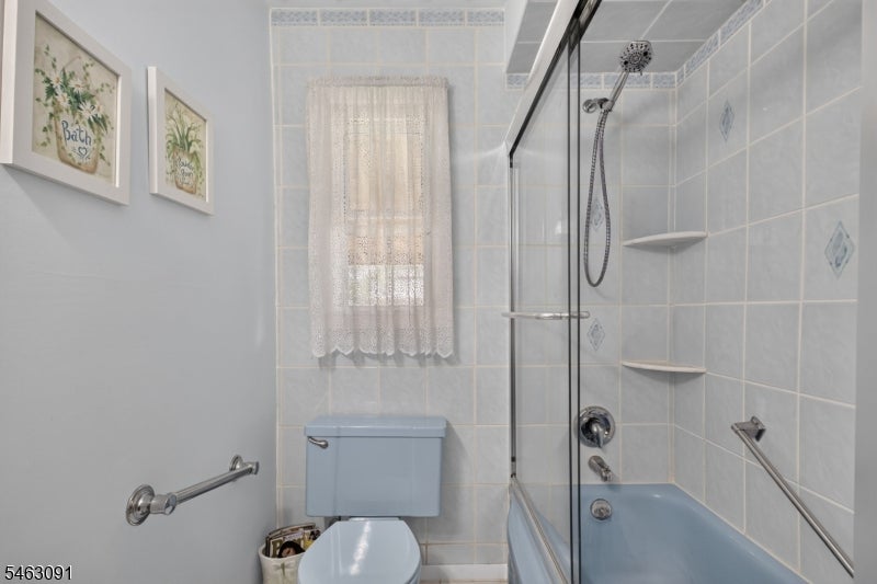 Bathroom with a blue bathtub and toilet, glass shower enclosure, and lace-curtained window.