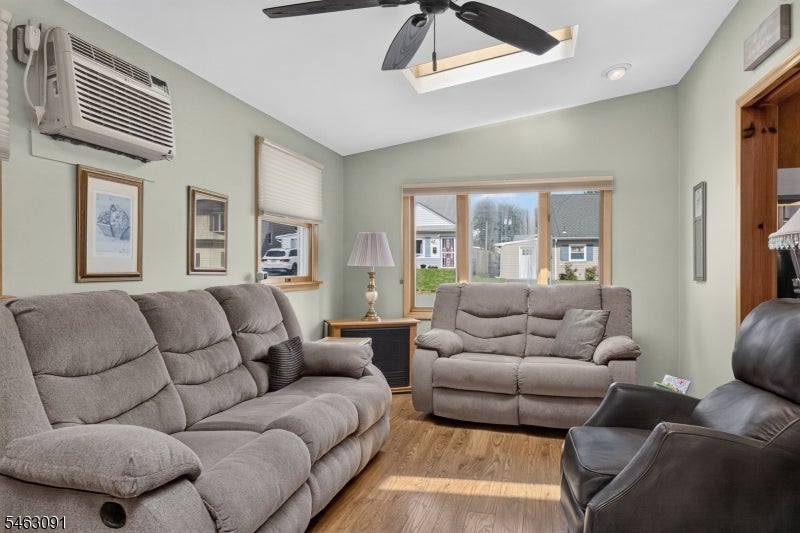 Living room with gray reclining sofas, a dark leather chair, and windows overlooking neighboring homes.