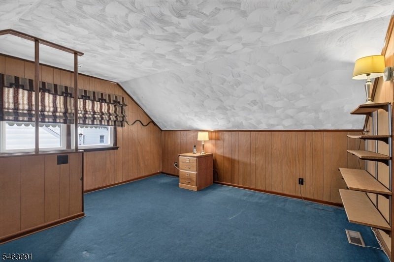 Finished attic room with blue carpet, wood paneling, and built-in shelves.