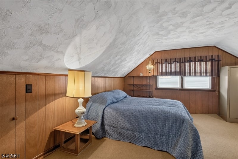 Bedroom with a blue-quilted bed, wood-paneled walls, and a low sloped ceiling.